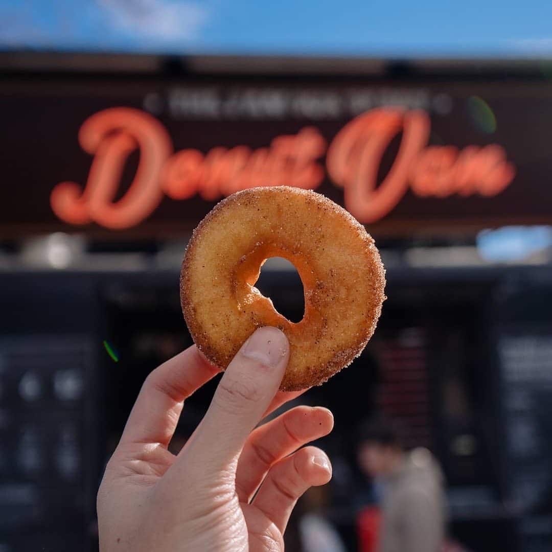 A hot cinnamon donut held up in front of the blurred Donut Van sign