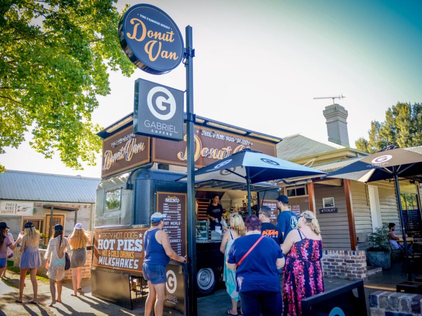 The Donut Van in its earlier brown livery, umbrellas up and a crowd at the counter