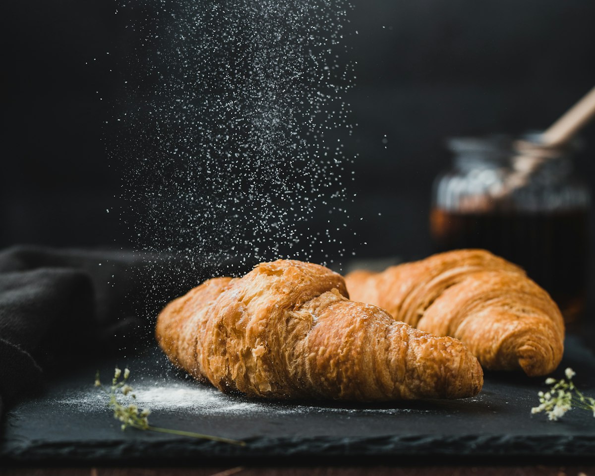 Golden croissants being dusted with icing sugar on a slate board