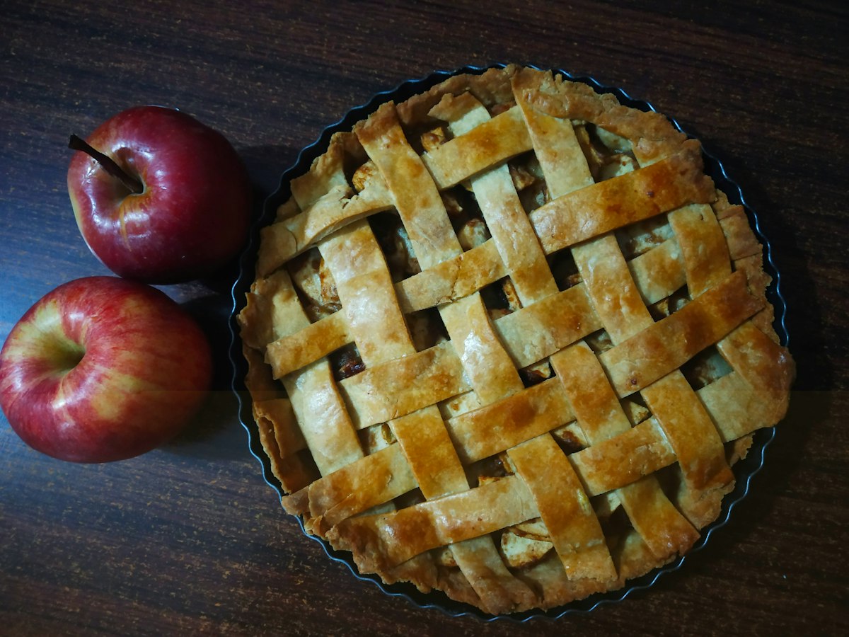 A golden lattice-topped fruit pie fresh from the oven, with apples beside it
