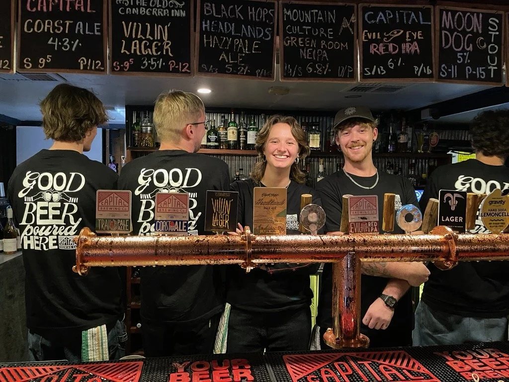 The inn's bar team behind the copper tap rail, with the chalked tap board above