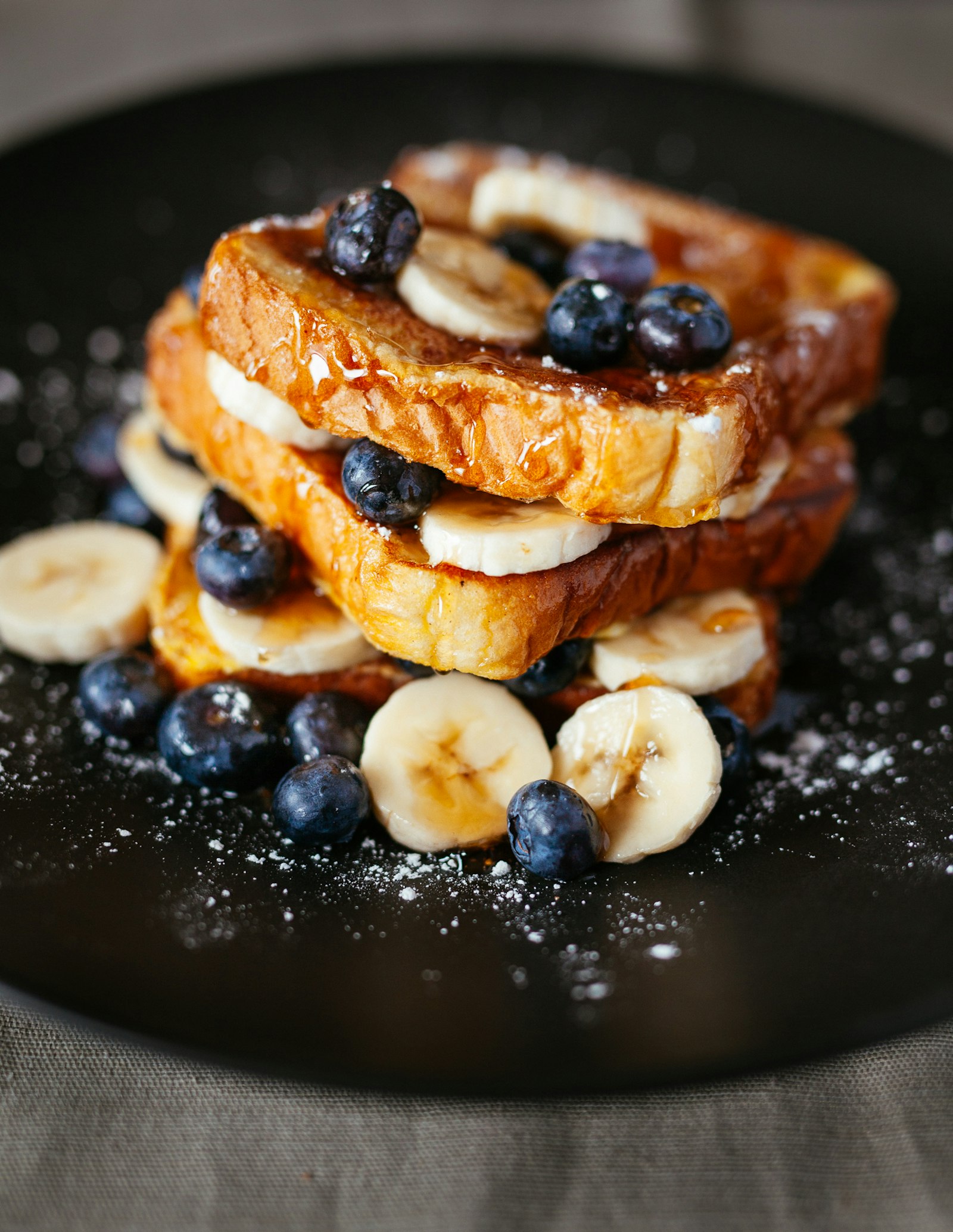 A tall stack of golden pancakes with banana and blueberries