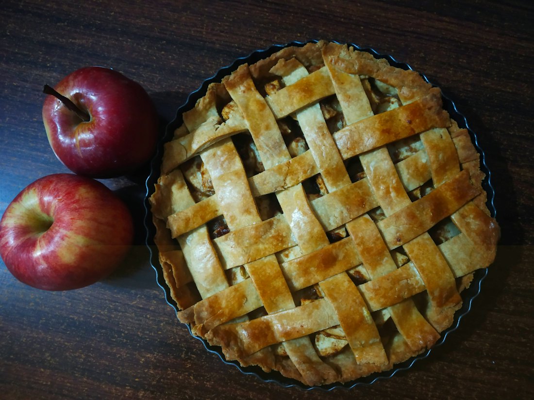 A golden lattice-topped pie fresh from the oven, with apples beside it