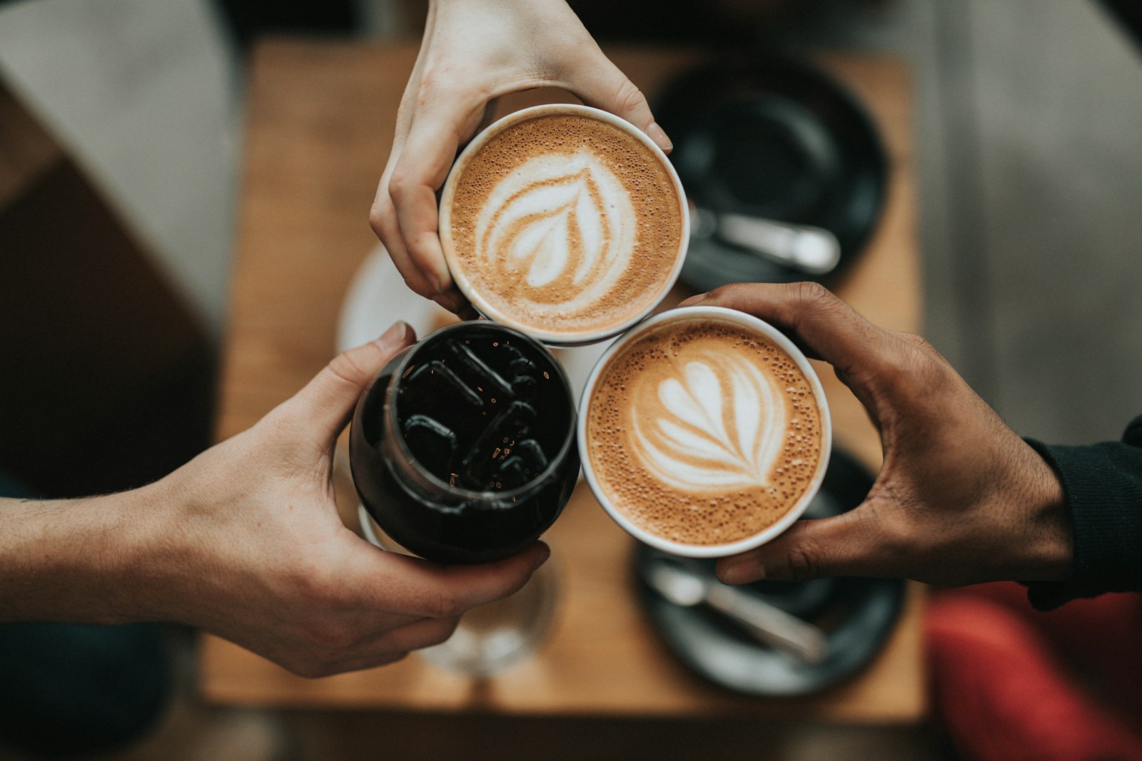 Friends raising latte-art coffees over a café table