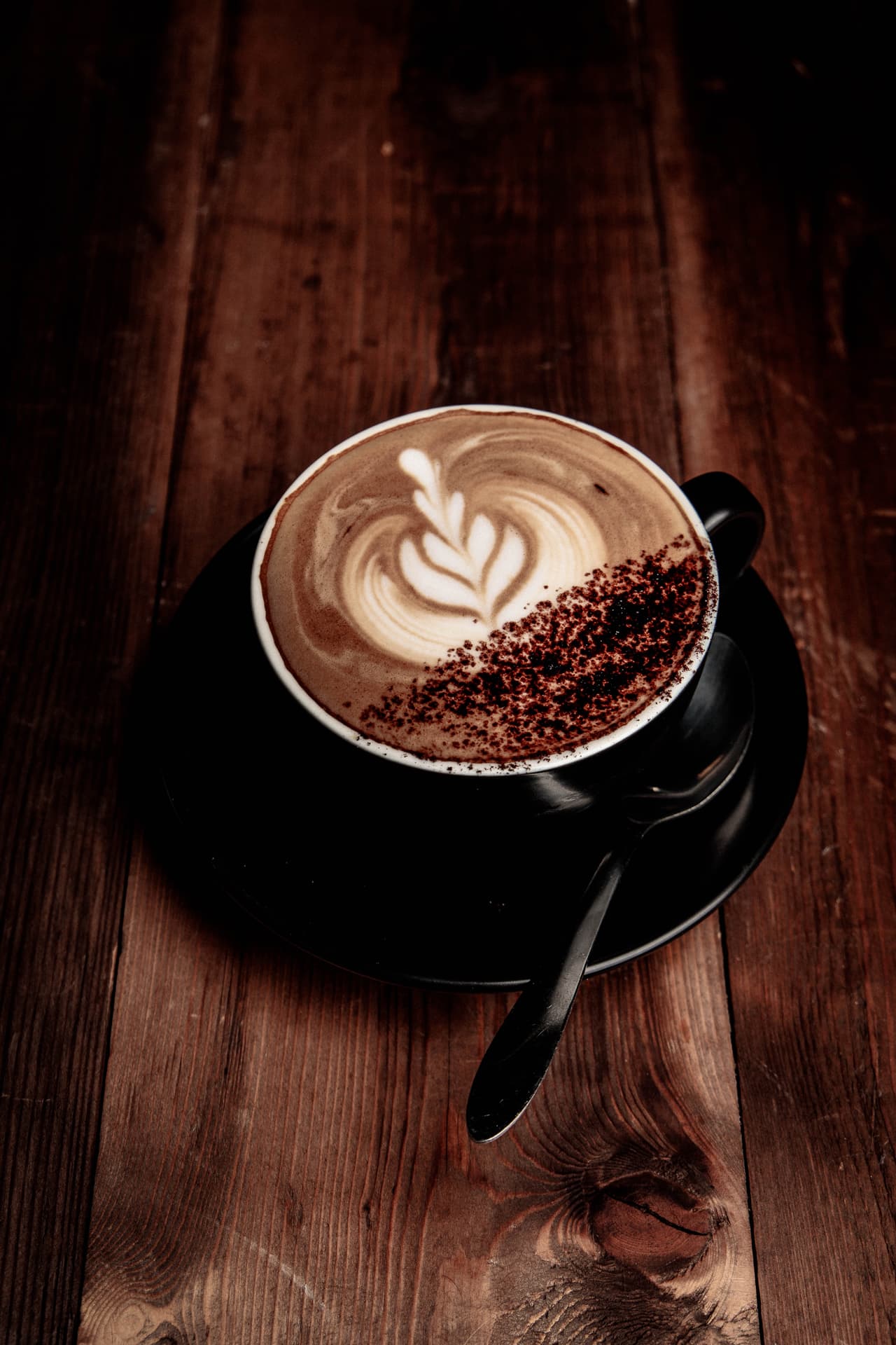 A flat white with latte art on a dark timber table at The Turret Cafe